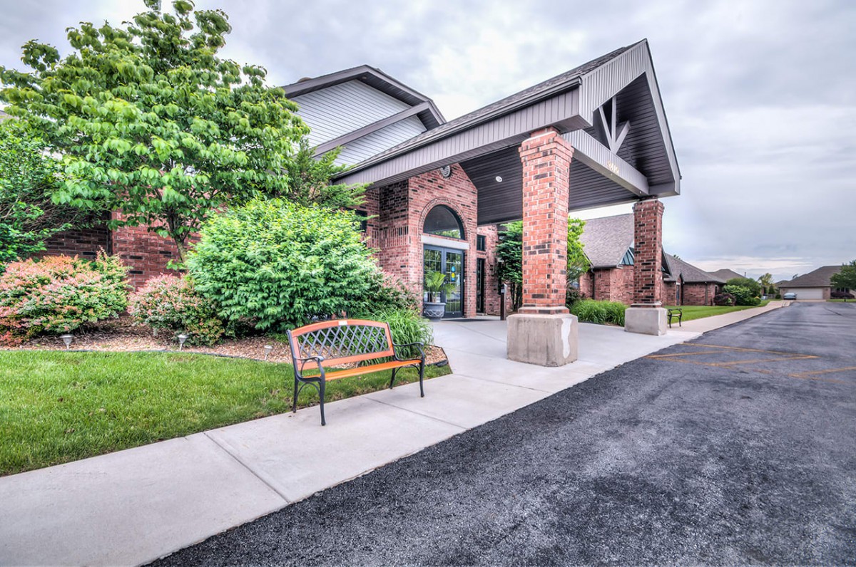 A brick building entrance with a bench and landscaped greenery.