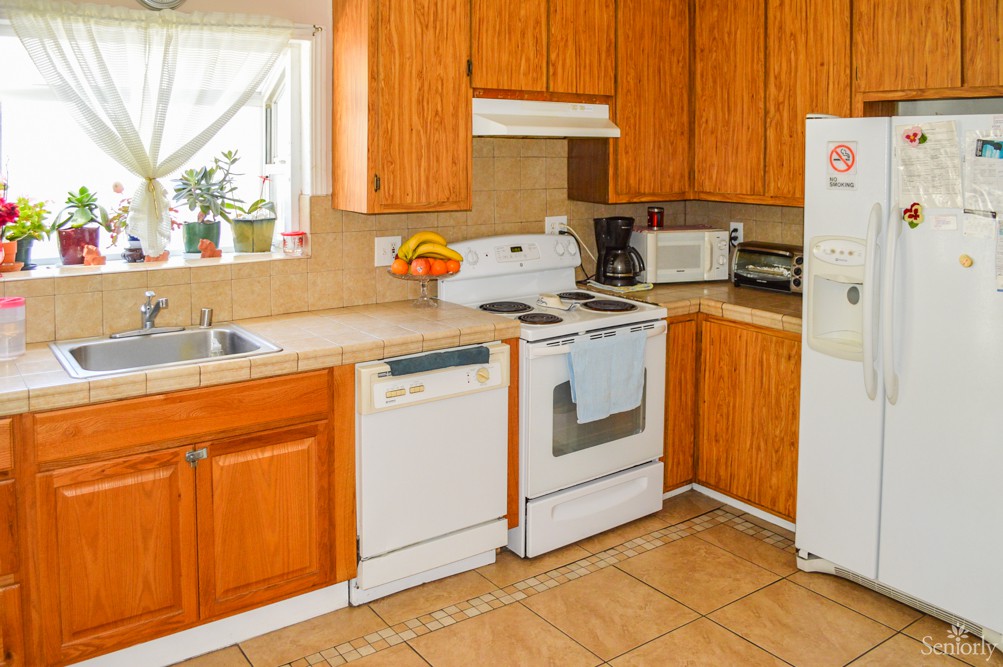 A cozy kitchen featuring wooden cabinets, various appliances, and a tiled floor.