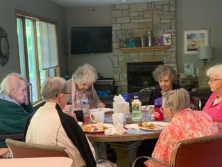 A group of elderly people enjoying a meal together around a table in a cozy living room.