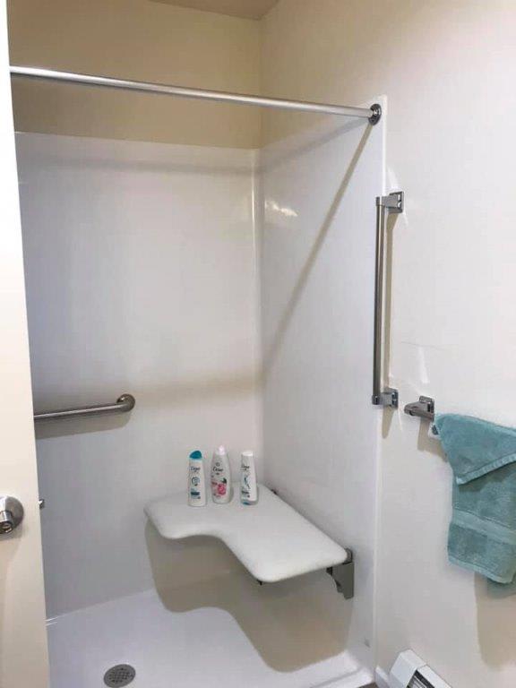 An accessible bathroom shower with a seat and handrails.