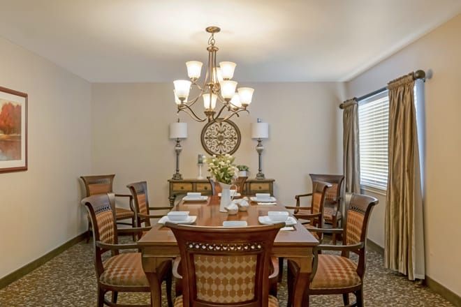 A well-decorated dining room featuring a large wooden table, elegant chairs, and a central chandelier.