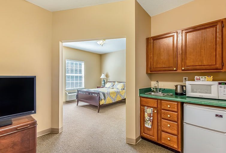 A cozy apartment interior featuring a kitchenette and a bedroom visible through an open doorway.