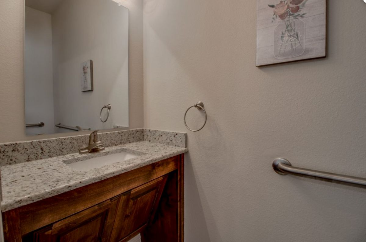 A bathroom featuring a sink with a marble countertop, mirror, towel ring, and wall artwork.