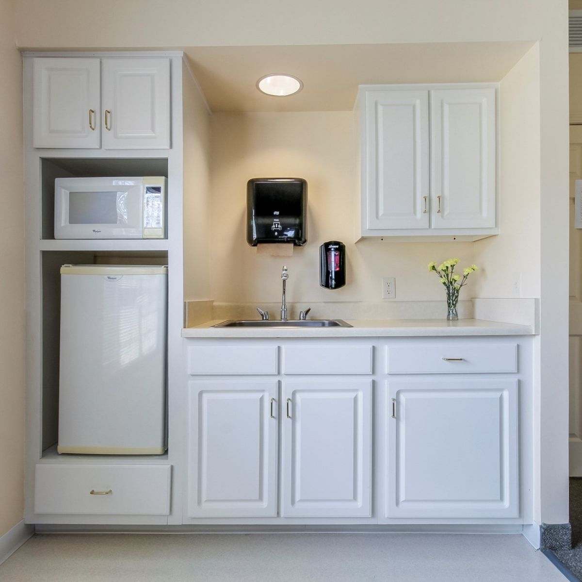 A minimalist kitchenette featuring white cabinets, a microwave, and a mini fridge.