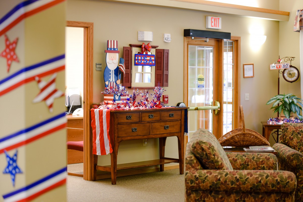 A living room decorated with American flags and patriotic themes, featuring a wooden sideboard and comfortable seating.