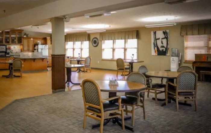 A spacious dining area with multiple tables and chairs, featuring large windows and decorated walls.