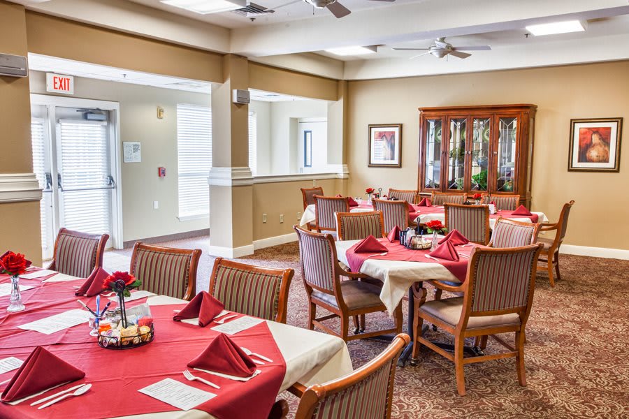 An elegantly set dining room with red tablecloths and neatly arranged chairs.