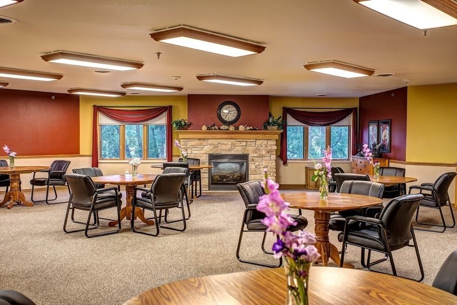 A cozy dining area with round tables and chairs, decorated with flowers and a fireplace.