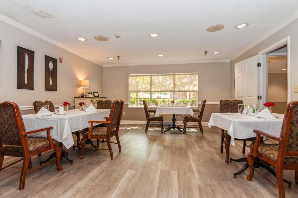 A cozy dining room with elegantly set tables and chairs, featuring a large window allowing natural light to fill the space.