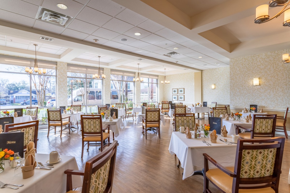 A spacious dining room with neatly arranged tables and chairs, featuring large windows that allow natural light to fill the space.