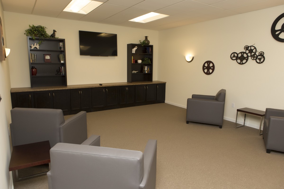 A modern lounge area featuring comfortable chairs, a wall-mounted television, and sleek shelving.