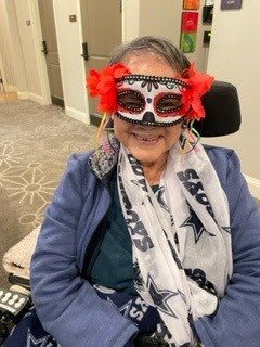 A person wearing a festive mask with red flowers and a patterned scarf, enjoying a celebration.
