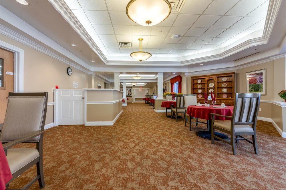 A spacious hallway with carpeted flooring, ceiling lights, and a cozy dining area with tables and chairs.