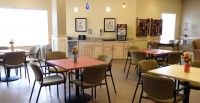 A photograph of a cafeteria with tables, chairs, and a kitchenette in the background.
