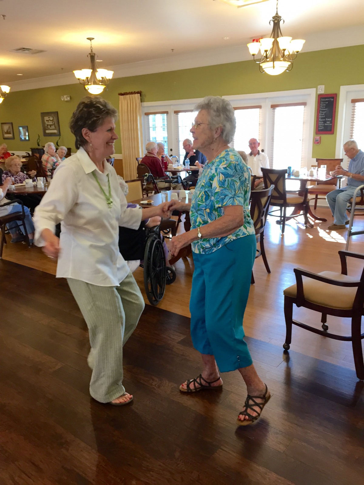 Two senior women joyfully dancing together in a community setting.