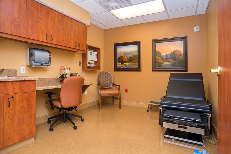 A well-organized doctor's office exam room with a desk, chair, and medical examination table.