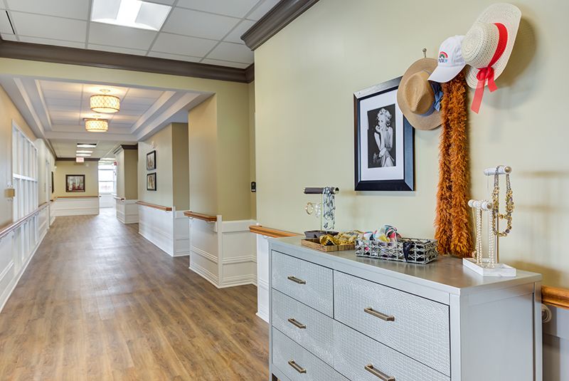 A hallway with wooden flooring, decorated with hats and a scarf on a dresser.