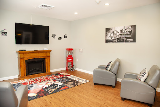 A cozy living room featuring a television, a fireplace, comfortable armchairs, and decorative wall art.