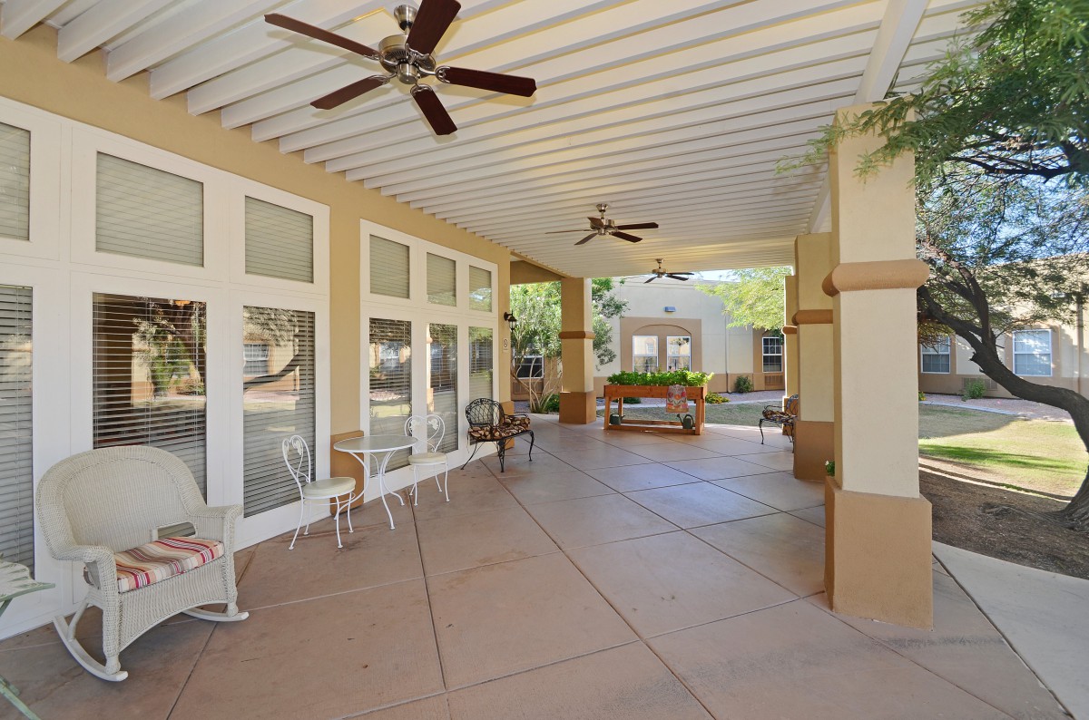 A spacious covered patio featuring ceiling fans, stylish outdoor furniture, and large windows overlooking a garden.