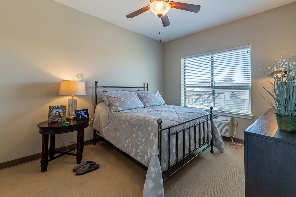 A cozy bedroom with a metal bed frame, nightstand, lamp, and ceiling fan.