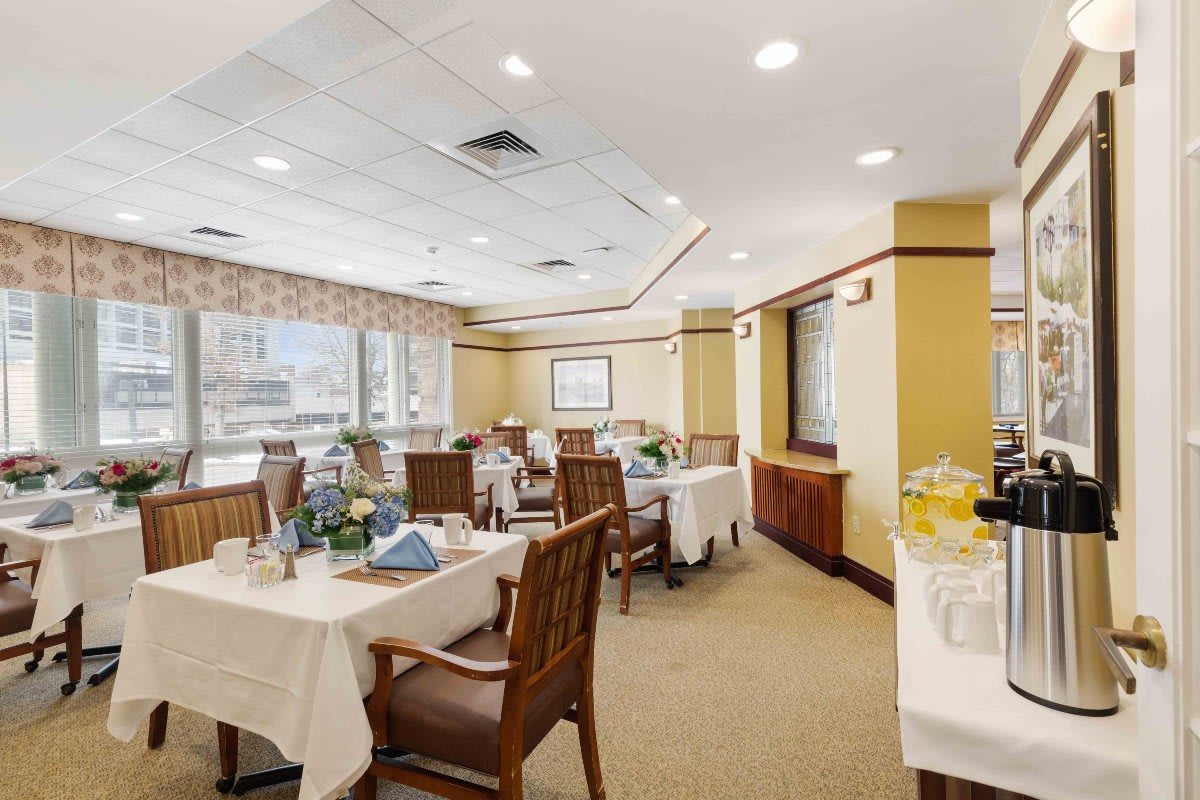 An elegant dining area with neatly arranged tables and chairs, well-lit by large windows.