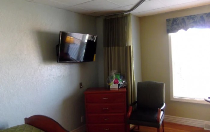 A hospital room with a wall-mounted television, dresser, and chair.