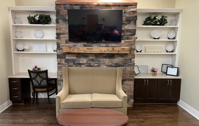 A cozy living room setup featuring a TV mounted above a stone fireplace, with a beige sofa and decorative shelving on either side.