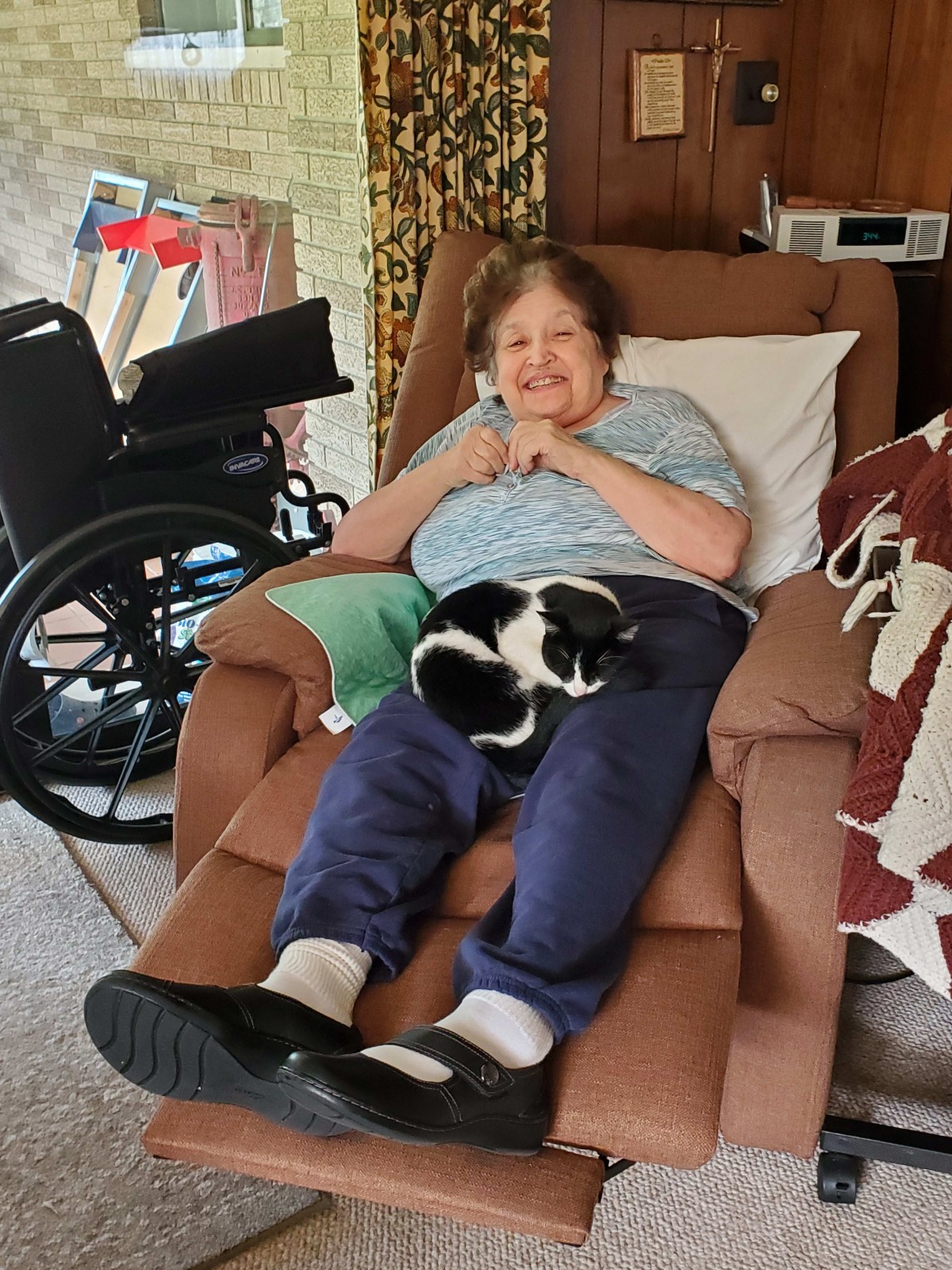 An elderly woman relaxing on a recliner with a black and white cat on her lap.