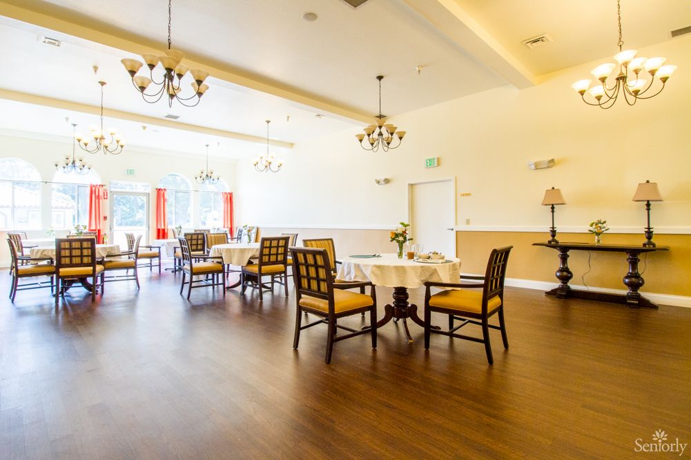A bright dining room with elegant chandeliers, wooden floors, and neatly arranged tables and chairs.