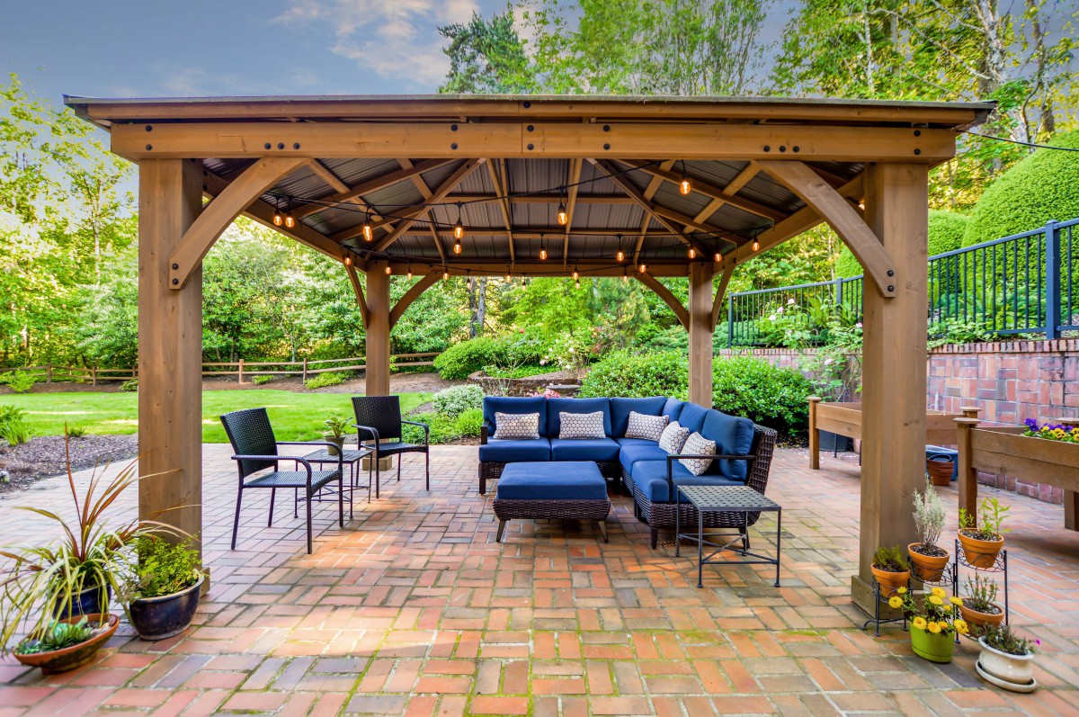 A cozy outdoor patio with a gazebo, featuring comfortable blue seating surrounded by lush greenery.