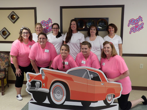 A cheerful group of women gathered for an event, all wearing pink shirts and posing with a fun orange car cutout.