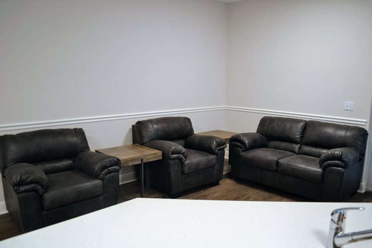 A cozy living room setup with dark leather sofas and small wooden tables against a neutral wall.
