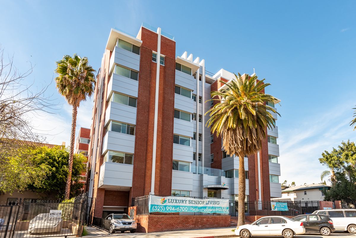 A brick apartment building with palm trees and parked cars in an urban setting.