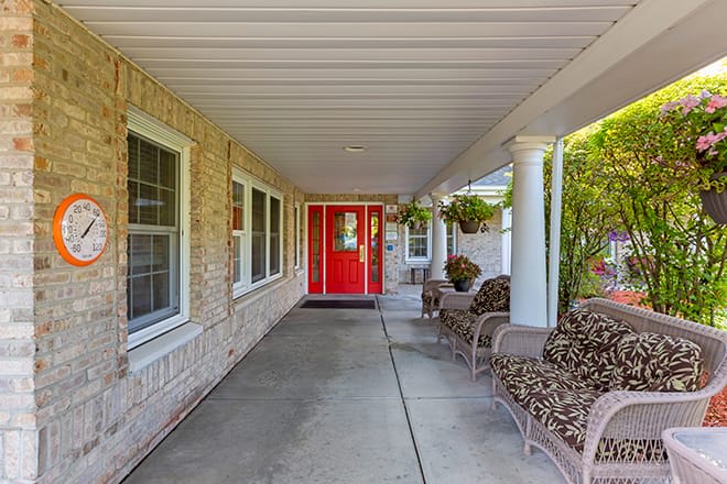 A welcoming front porch with a bright red door, featuring comfortable outdoor seating and decorative plants.
