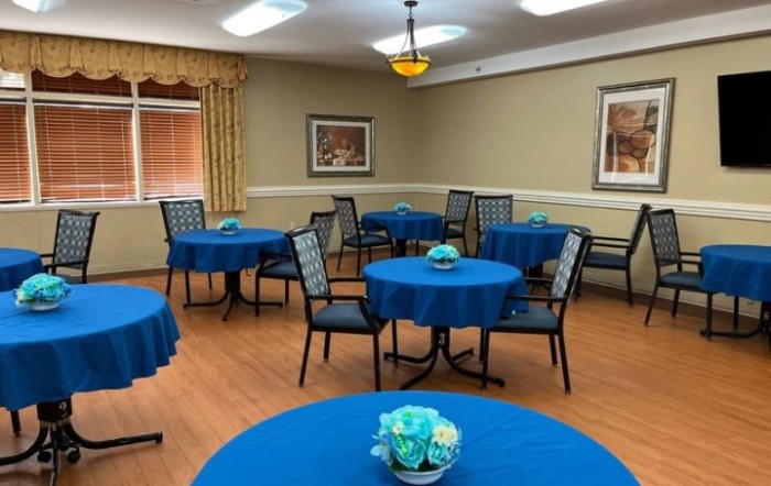 An empty dining room with round tables covered in blue tablecloths, each adorned with a floral centerpiece.