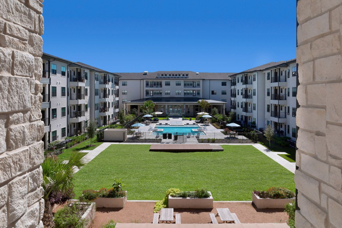 A modern apartment complex with a central courtyard featuring a swimming pool and a well-maintained lawn.