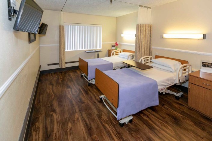 A hospital room with two beds and a curtain divider, featuring clean and organized interior design.