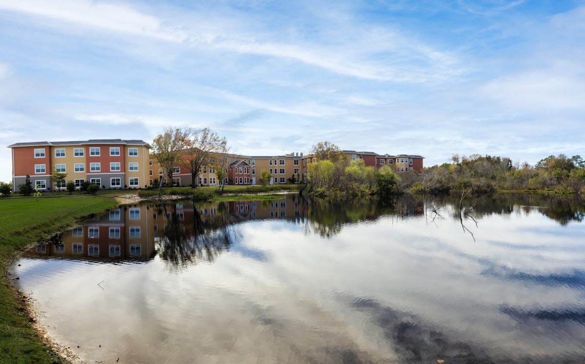 Scenic view of a river reflecting nearby buildings and trees under a blue sky.