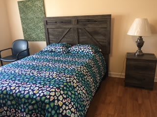 A bedroom featuring a bed with colorful bedding, a wooden headboard, and a nightstand with a lamp.
