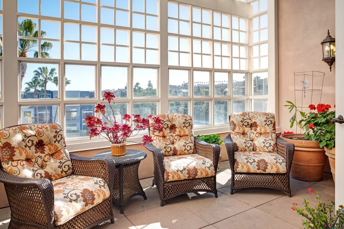 A sunlit room featuring wicker chairs with floral-patterned cushions, surrounded by large windows.