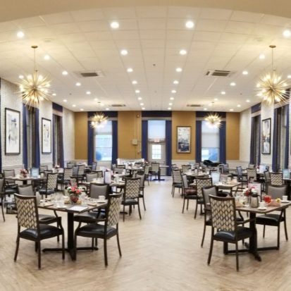 An elegant dining room with neatly arranged tables and chairs, illuminated by chandeliers.
