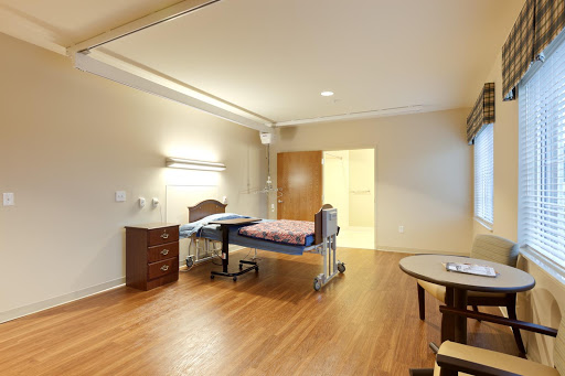 A well-lit hospital patient room featuring a single bed, wooden flooring, and essential furniture.