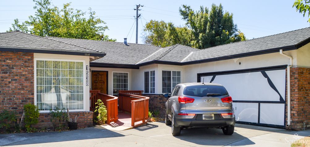 A single-story house with a driveway, car, and garage under a sunny sky.