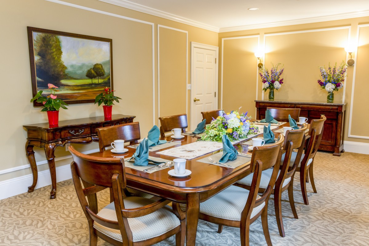 A formal dining room setup with a wooden table, surrounded by chairs and adorned with elegant decor and a vase of flowers.