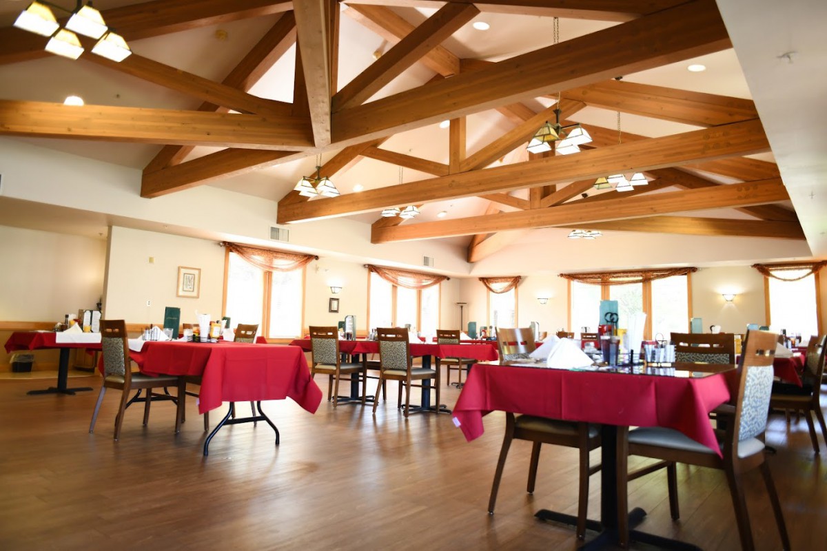 A spacious restaurant dining room featuring red tablecloths and wooden beam ceilings.