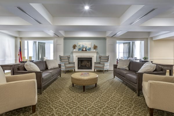 A spacious and elegantly decorated living room featuring a fireplace, sofas, chairs, and a central coffee table.