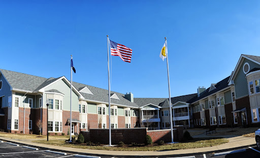 A view of a residential facility with the American flag and a state flag flying in front under a clear blue sky.