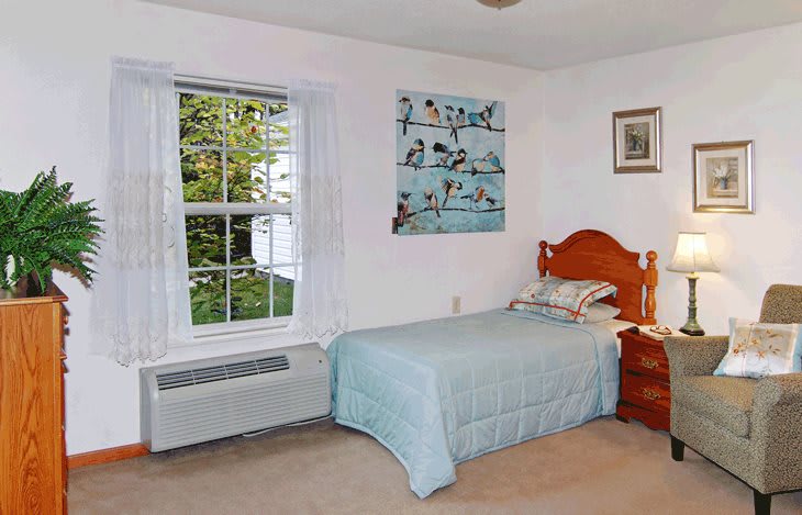 A cozy bedroom with a single bed beside a window, featuring wall art and a nightstand with a lamp.