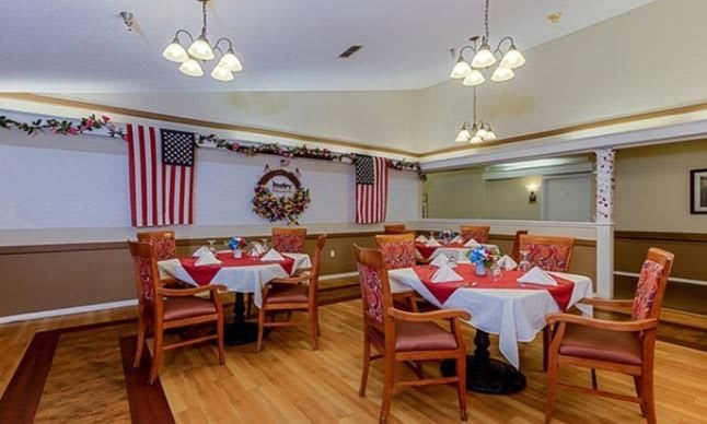 A warmly decorated dining area features tables set with red and white linens, American flags, and a wreath adornment.