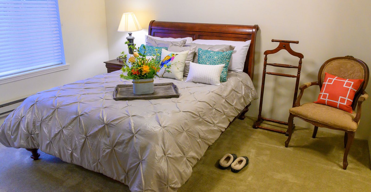A cozy bedroom setting with a neatly made bed featuring decorative pillows and a floral arrangement on a tray.